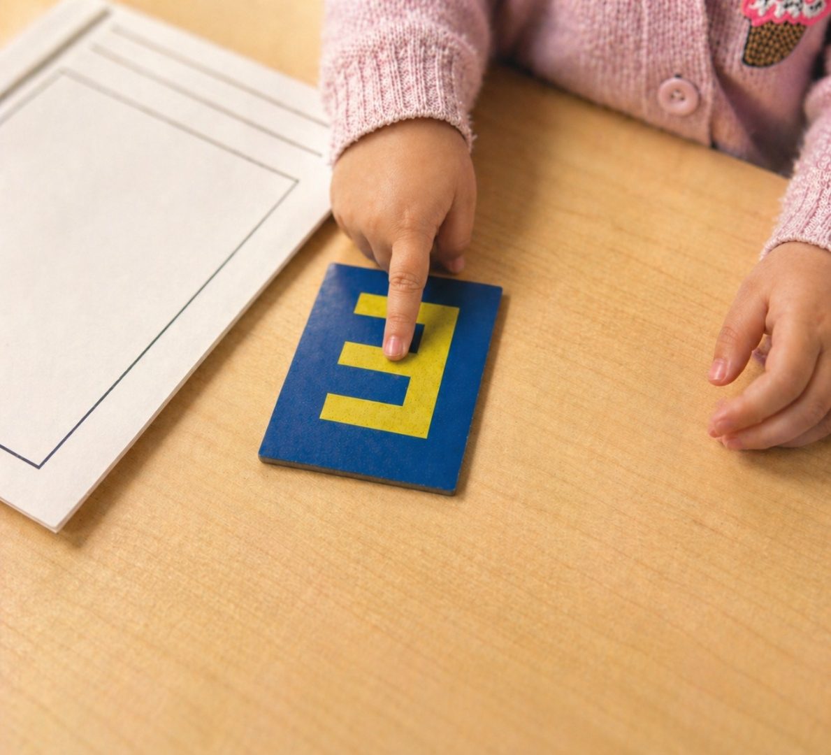 A young child tracing a sandpaper letter E with their finger on a wooden table