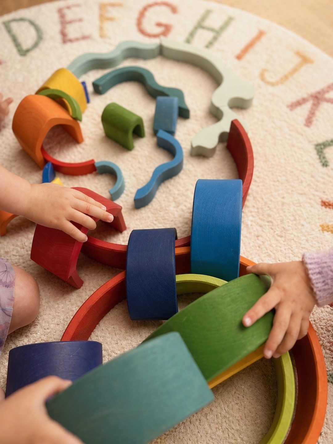 Two children playing together with rainbow stacking arches on an alphabet rug