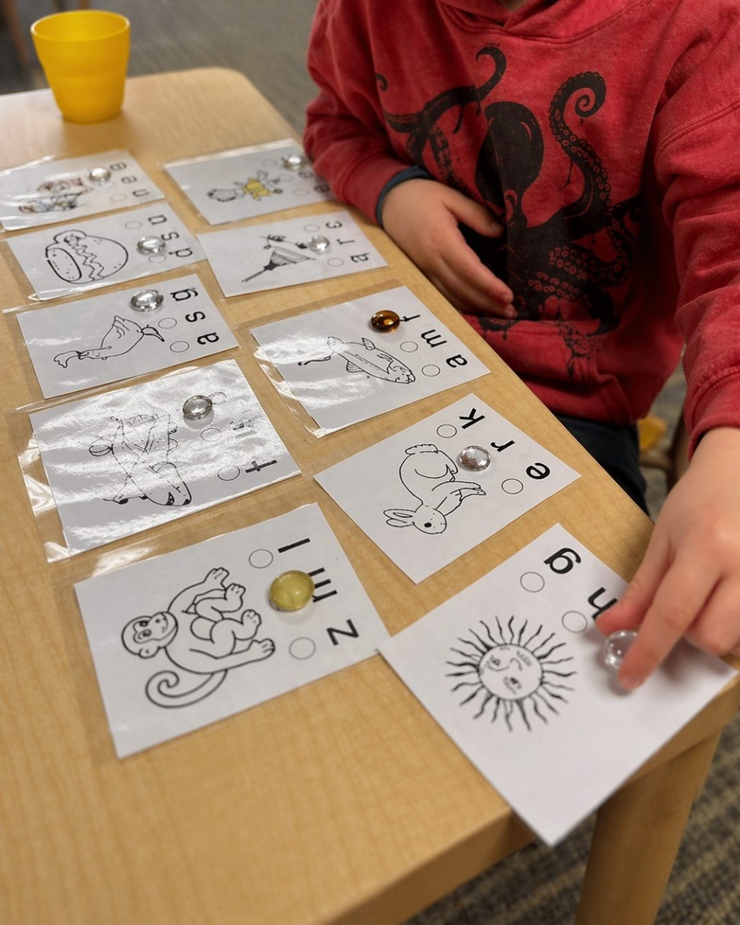 A child working with picture cards and glass gems to match initial sounds to letters